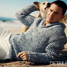 a man laying on the beach next to his dog wearing a knitted sweater and hat