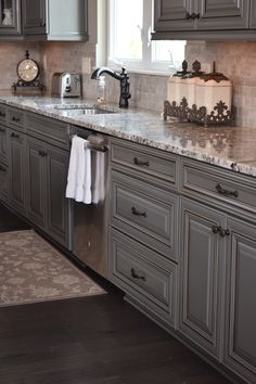 Speckled gray and white granite countertops with gray melburne style cabinets. Dark hardwood floors and dark cabinet hardware. Light Gray Kitchen Cabinets With Dark Granite Countertops, Kitchen With Dark Gray Floors, Gray Cabinets Dark Floors, Grey Cabinets Dark Floors, Dark Floor Grey Cabinets, Gray Kitchen Countertops Granite, Gray Cabinets Dark Countertops, Light Gray Cabinets With Dark Countertop, Grey Cabinets With Dark Floors