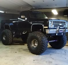 a black truck parked in a garage next to a giant tire on the floor and an advertisement that reads, and on the 8th day, god made a square body