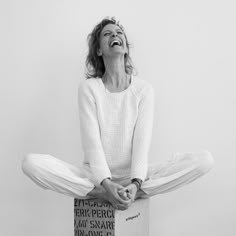 a woman sitting on top of a box with her eyes closed and hands in the air