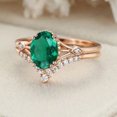 an oval green gemstone surrounded by white diamonds sits atop a rose - shaped ring