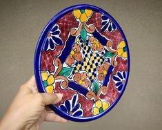 a hand is holding a colorful plate with flowers on the front and sides, which are painted in bright colors