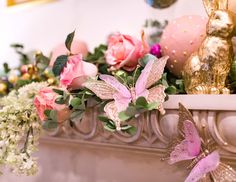 pink and white flowers are on the mantle in front of gold decorations, such as butterflies