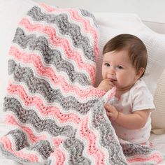 a baby is sitting on a bed under a crocheted blanket