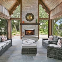 an outdoor living area with wicker furniture and fireplace in the center surrounded by large windows