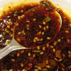 a spoon is full of sauce on a white plate with sesame seeds in the bowl