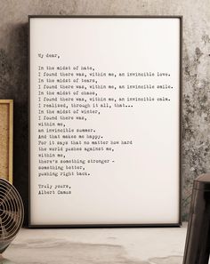 a framed poem on a wall next to a fan and a table with a vase