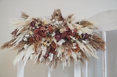 an arrangement of dried flowers and feathers on a white chair with a wall in the background