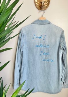 a blue jean jacket with writing on it hanging from a wall next to a potted plant