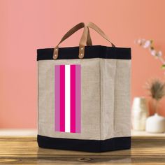 a pink and white striped bag sitting on top of a wooden table next to a vase