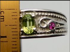 Hi The center stone of this ring is a natural earth mined, peridot, 6x4 mm , oval shape, v v s clarity, The stones on the sides are 2 natural earth mined rubies, 1.5mm round shape, 0.04 ctw, v s clarity. The ring is made in 14k solid gold and the weight is 7 grams. I have 3 of this rings, one in white, one in yellow and one in Rose gold. The size of the rings is 7.75. I offer free sizing for this rings to any size that you need. If you are getting one of this rings please send me a message to le Diamond Bows, Ruby Diamond Rings, Bow Ring, Natural Earth, Gold Work, Ruby Diamond, Ruby Ring, Free Size, Deep Purple