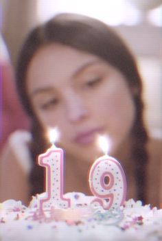 a girl blowing out the candles on her birthday cake that is decorated with pink and white icing