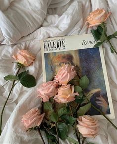 some pink roses laying on top of a white sheet and an open book with the cover pulled down