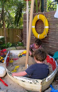 two young boys playing in an outdoor sand pit with life preservers and toys on the ground