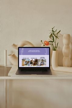 an open laptop computer sitting on top of a white table next to vases and flowers