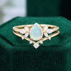 an opal and diamond ring sits on top of a green velvet cushioned box