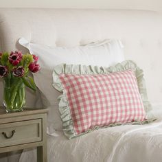 a white bed topped with pillows next to a vase filled with pink and green flowers