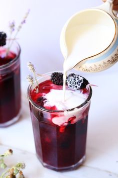 a pitcher pouring milk over a glass filled with blackberry ice cream and blackberries on the side