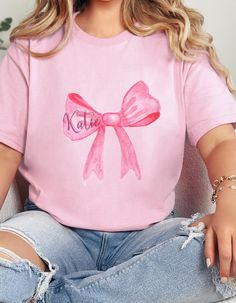 Pink bow custom name coquette tshirt for her gift for student grandmillenial tee vintage retro bow t-shirt  Made with medium fabric (5.3 oz/yd² (180 g/m consisting of 100% cotton for year-round comfort that is sustainable and highly durable.  The classic fit of this shirt ensures a comfy, relaxed wear while the crew neckline adds that neat, timeless look that can blend into any occasion, casual or semi-formal. The tear-away label means a scratch-free experience with no irritation or discomfort w Trendy Customizable Pink T-shirt, Personalized Summer T-shirt For Gift, Personalized T-shirt For Spring Gift, Personalized Pink T-shirt For Summer, Pink Personalized Short Sleeve T-shirt, Personalized Pink Short Sleeve T-shirt, Casual Personalized Pink T-shirt, Cotton T-shirt With Pink Bow, Short Sleeve, Personalized Casual Short Sleeve T-shirt