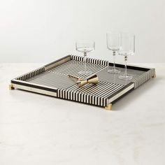 two wine glasses sitting on top of a black and white striped tray with gold handles