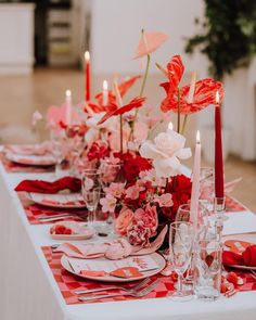 a long table is set with red and white flowers, candles, and napkins