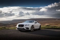 a white car parked on the side of a road in front of some hills and clouds