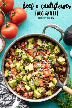 a skillet full of taco salad with tomatoes and avocado