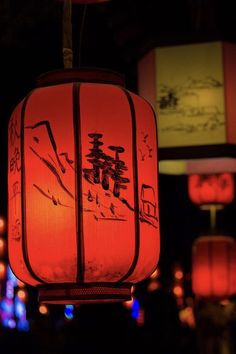 red lanterns lit up in the dark with chinese writing on them and lights behind them