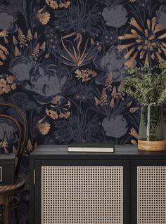 a black and gold floral wallpaper with wicker sideboard next to a chair