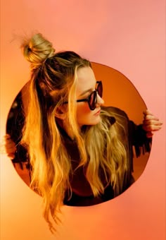 a woman with long blonde hair and sunglasses looking into a round mirror in the shape of a cat's head