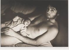 a man holding a baby in his arms while laying on a bed with the other arm around him