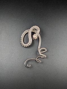 Intricate silver-plated woven wire and a manmade pink opal pearl create a twisting illusion of a snake clinging to your ear. A shimmering iridescent pale pink 'opal' resides in the head of this left side only ear cuff.  This serpent ear cuff has been polished to a bright silver shine and clear coated. The design for this ear cuff was inspired by a Lan Anh Handmade video. No piercings are required to enjoy wearing this ear cuff. The serpent's coils wrap around your outer ear using gentle tension and friction to hold the cuff in place. The cuff is around 2 1/4 inches in height and 1 3/8 inch in width. Silver Snake-shaped Party Earrings, Silver Wire Wrapped Ear Cuff For Party, Party Silver Wire Wrapped Ear Cuff, Elegant Silver Spiral Ear Cuff, Silver Spiral Adjustable Ear Cuff, Sterling Silver Snake-shaped Jewelry For Parties, Sterling Silver Snake Shape Jewelry For Party, Elegant Silver Snake-shaped Earrings, Silver Spiral Jewelry For Party