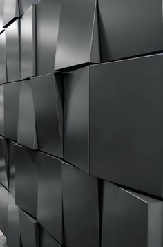 a man walking down a sidewalk next to a wall covered in black cube shaped tiles