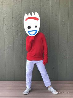 a person in a red shirt and white pants with a mask on their head standing next to a wall