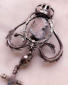 During the Georgian era, when new sources of silver were found in silver-rich South America, the production of silver jewelry flourished. Silver was the most popular type of metal for making jewelry in Europe at the time and has remained one of our most prized jewelry-making materials to this day. Wrought with symbolism, this unreal example features a customized drop of symbolism including a heart, a cross, an anchor, and a steel-cut anchor. The top element features a large crown and laurel leav Baroque Jewelry With Historical Design For Formal Occasions, Baroque Historical Jewelry For Formal Occasions, Baroque Historical Design Jewelry For Formal Occasions, Elegant Silver Jewelry In White Bronze, Ornate Baroque Jewelry For Anniversary, Elegant Baroque Silver Jewelry, Antique Silver Baroque Style Jewelry, Antique Silver Baroque Jewelry, Victorian Baroque Engraved Jewelry