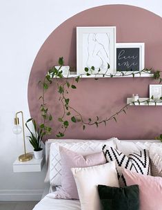 a bed topped with lots of pillows next to a pink wall