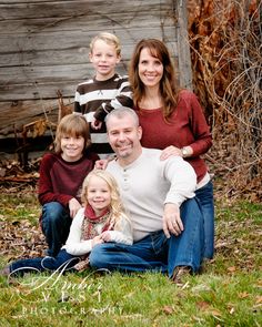 a family sitting on the grass in front of a wooden fence with their two children