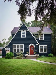 a blue house with white trim and red door in the middle of a grassy yard