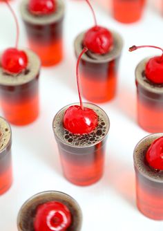 small cups filled with liquid and cherries on top of each other, sitting next to each other