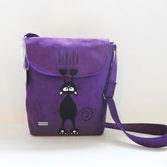 a purple purse with a black cat on it's front and shoulder strap, sitting against a white wall