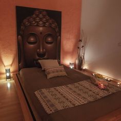 a large buddha head is on the wall above a bed with decorative pillows and blankets