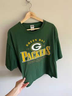 a green bay packers t - shirt hangs on a hanger in front of a white wall