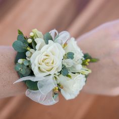 a wrist corsage with white flowers and greenery on it's arm