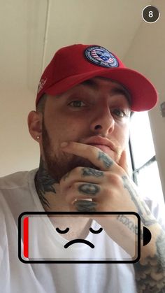 a man with tattoos and a red hat is looking at the camera while holding his finger to his mouth