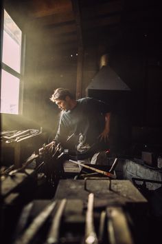 a man is working on some wood in the dark with sunlight coming through the window