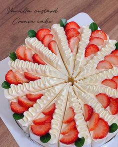 a cake decorated with strawberries and leaves on a white plate sitting on a wooden table