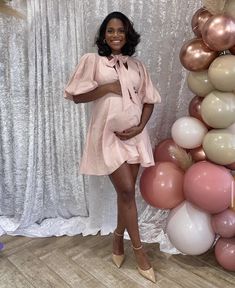 a pregnant woman standing in front of balloons with her hands on her hip and smiling at the camera