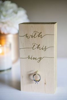 a wooden box with a ring on it sitting next to a candle and some flowers