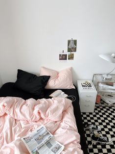 a black and white checkered floor with a bed covered in pink sheets, pillows and blankets