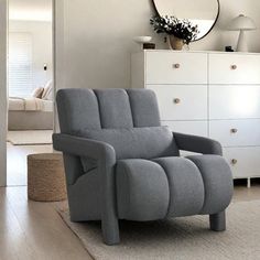 a grey chair sitting on top of a wooden floor next to a white dresser and mirror